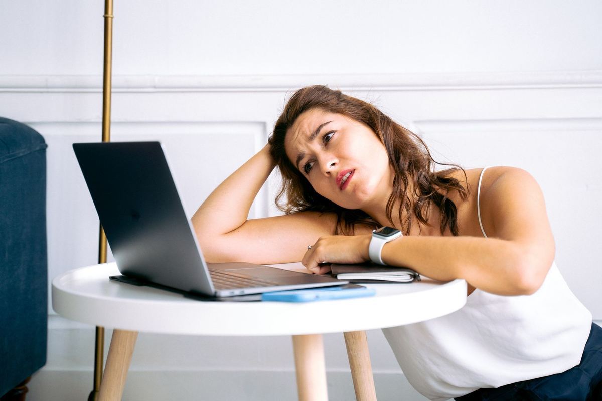 A woman leaning over a laptop with a frustrated expression while waiting for something to load