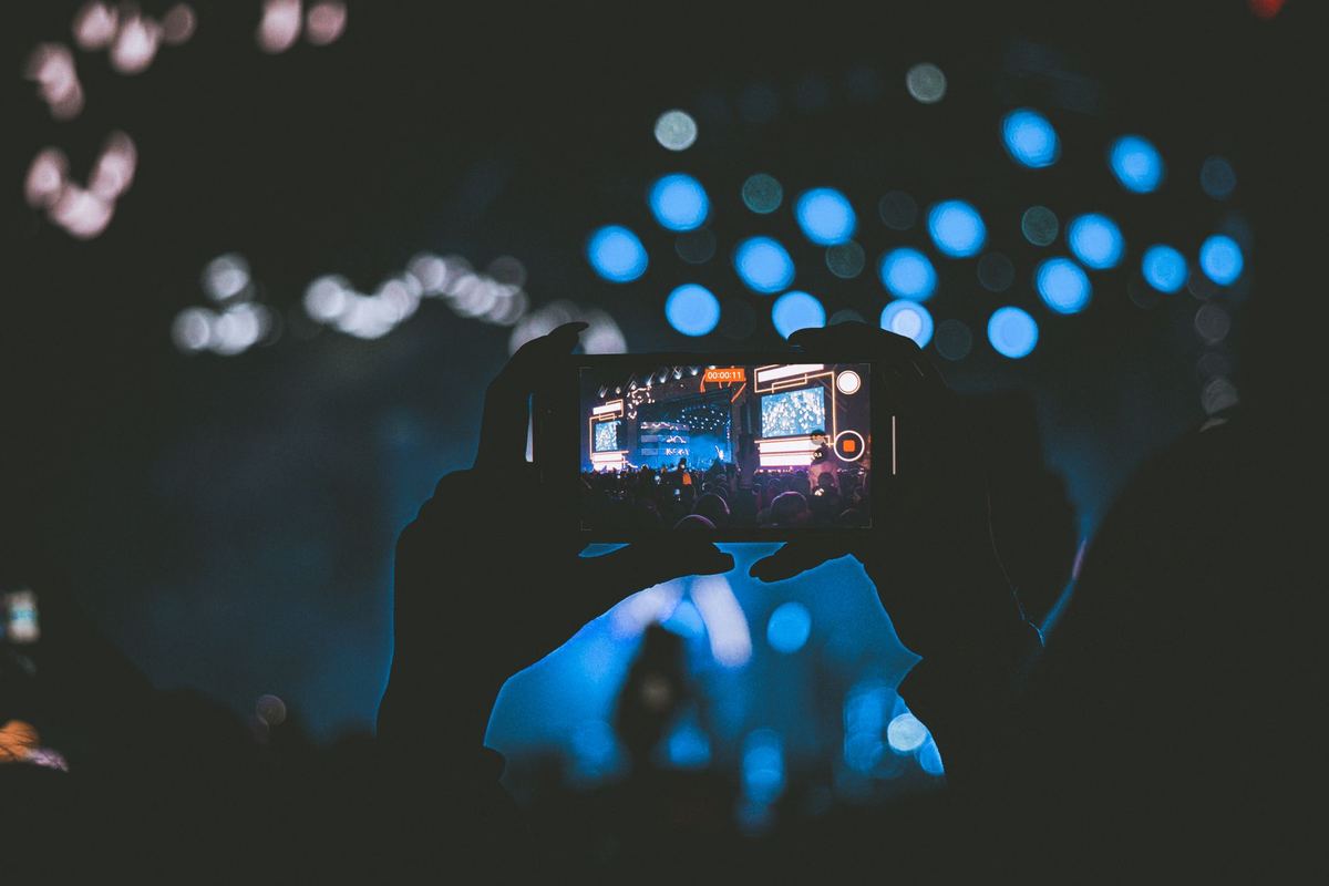 A hand holding up a phone recording a long video at a live event