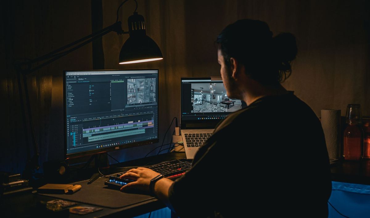 A video editor reviewing footage across two monitors at night